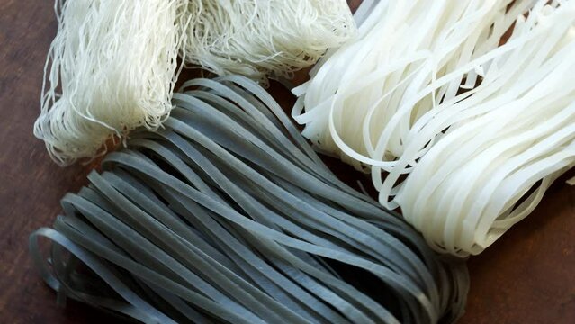 Rice noodles of three different types set uncooked. Close-up view, table spin.