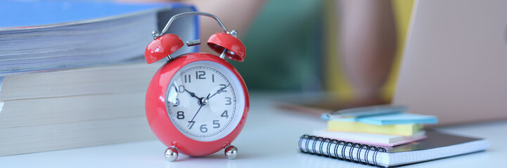 Woman sits at workplace next to alarm clock at ten in morning