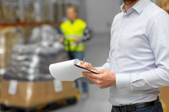 logistic business, shipment and people concept - close up of businessman with clipboard at warehouse