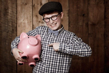 Saving is what its all about. Young boy in retro clothing holding his piggybank while pointing...