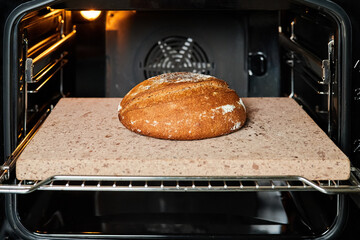Homemade round rye bread is baked in the oven on a baking stone. Close-up, selective focus