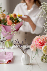 people, gardening and floral design concept - lavender flowers in vase on table over happy smiling woman or floral artist with bunch of flowers working at studio