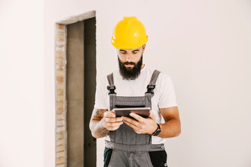A painter standing in building in construction process and using tablet.
