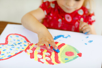Little creative toddler girl painting with finger colors a fish. Active child having fun with...