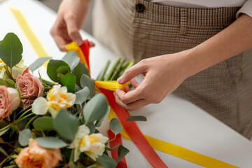 people, gardening and floral design concept - close up of woman or floral artist making bunch of flowers at studio