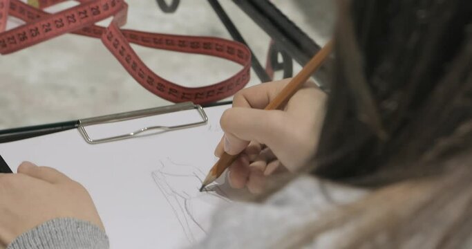 the designer draws a sketch of an evening dress with a pencil on a transparent table near the measuring element. creating a design for a wedding dress at the factory. close-up
