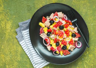 Remojon salad of blood oranges, potatoes, boiled salted fish and red onions on a black plate on a green concrete background. Spanish cuisine.
