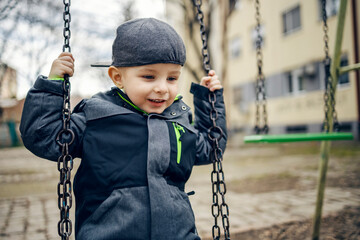A happy boy playing with swing on a playground.