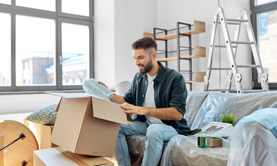 moving, people and real estate concept - happy smiling man unpacking boxes at new home