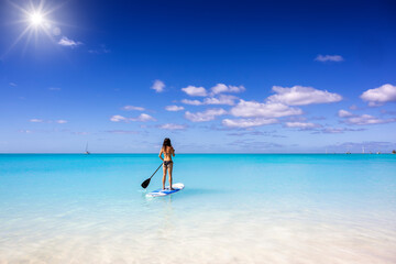 A woman exercising on a stand up paddle (SUP) board on turquoise, tropical sea