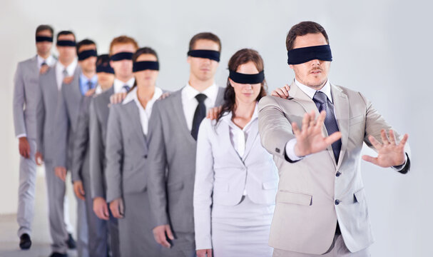 Blind leadership. A row of blindfolded businesspeople following a blindfolded leader.