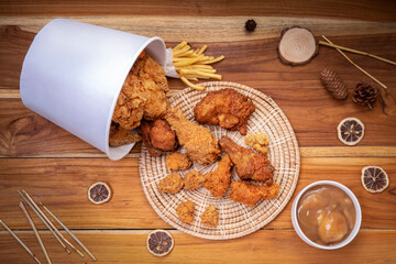 Fototapeta premium Fried chicken and french fries in paper bucket on wooden background, Deep fry Chicken and nuggets on wooden table. 