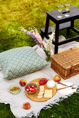 leisure, food and drinks concept - close up of snacks, wine and picnic basket on blanket on grass