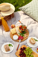 leisure, food and drinks concept - close up of snacks and picnic basket on blanket on grass at summer park
