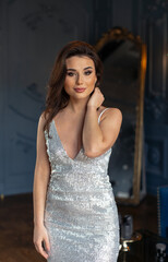 Fototapeta premium Beautiful brunette in a silver dress posing in a classic interior