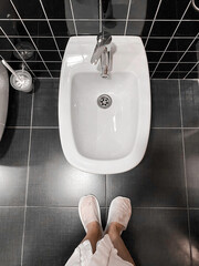 White bidet screwed to black tiles. girl in disposable slippers stands near a disinfected toilet