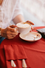 a woman sits at a table in a cafe, holding a white cup of aromatic coffee in her hands