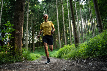Junger dunkelh&auml;utiger Mann in Sportkleidung l&auml;uft in der Natur im Wald