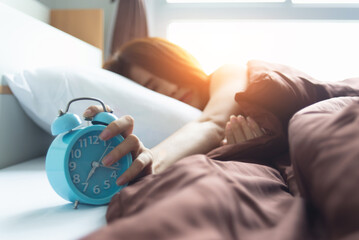 Young sleeping woman and alarm clock in bedroom at home, soon to wake up for sleeping attractive young woman with alarm clock.
