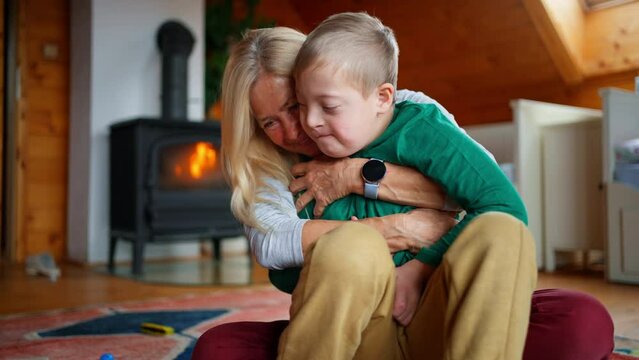 Happy boy with Down syndrome sitting on floor and hugging with his grandmother at home.