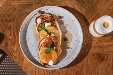 Appetizing delicious pancakes on a white plate with maple syrup, blueberries and mint on a beautiful wooden table.