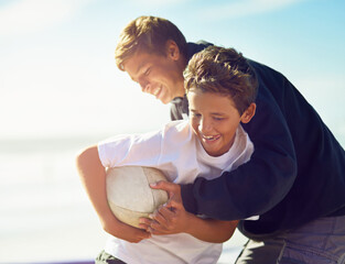 Just a friendly game between brothers. Shot of two happy brothers playing with a rugby ball on the beach.