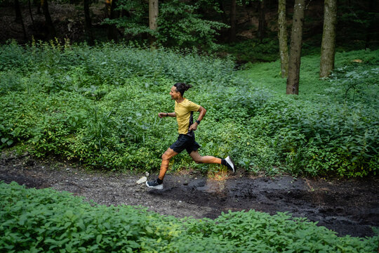 Junger dunkelhäutiger Mann in Sportkleidung läuft in der Natur im Wald