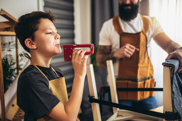 Smiling father is teaching his son upholstery at home, having fun.