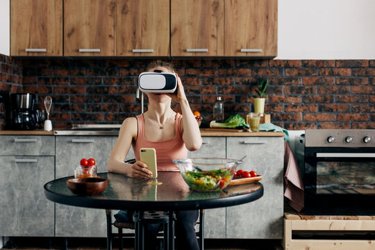 Athletic young woman in a virtual reality headset at home in her kitchen orders food, smart home, virtual reality