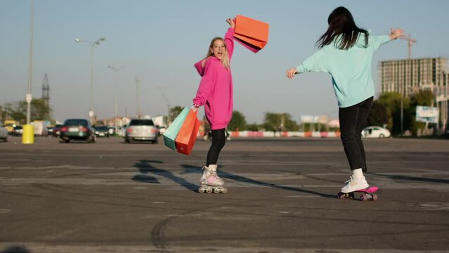 Two young girls on roller skates and a skateboard meet in a parking lot and happily embrace. Two girls joyfully meet each other.