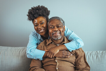 Smiling young woman sitting on sofa with happy older retired 70s father, enjoying pleasant...