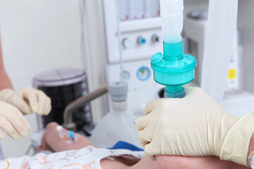 The resuscitator holds an oxygen mask on the child's face. The face is out of focus.Surgery under...