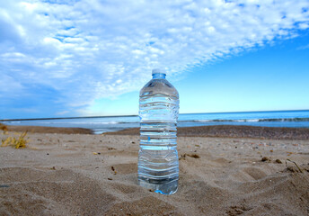 Plastic bottle with mineral water on beach by sea. PET bottle on the sand. Plastic trash thrown into the ocean. Thirst for water during dry and hot weather. Clean water in bottle at coastline.