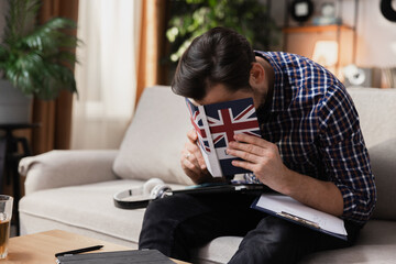 A man tries to memorize new English words. He is sitting on the couch in the living room and holding a dictionary in his hands.