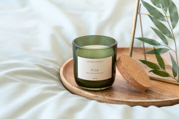 Green scented candle, golden photo frame with green leaves and wooden tray stand on bed with green linen.