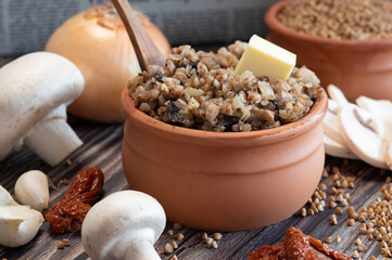 Buckwheat porridge with mushrooms and onion in a ceramic pot on the table