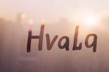 Slovenian and Croatian word Hvala thanks in english are painted on wet orange sunrise glass of...