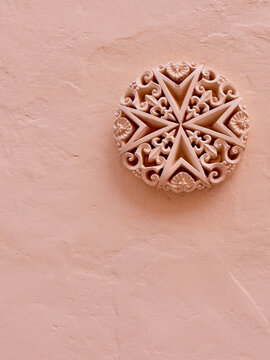 Detailed stucco heraldic emblem of Malta on rough painted wall of pastel colour. Vertical photo