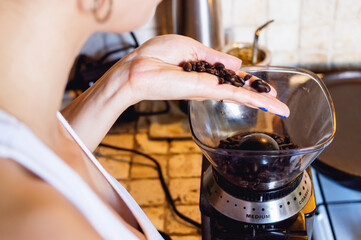 young caucasian woman in the kitchen pouring coffee beans in an electric grinder