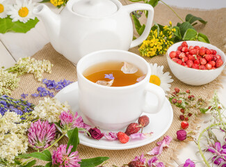 Herbal tea with rosehip, chamomile and clover in a white cup on a wooden table with flowers