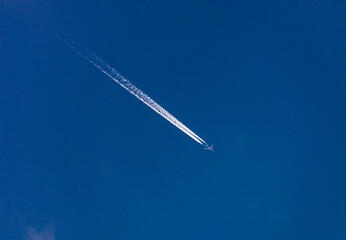 Route of an airplane with white contrail in the blue sky.