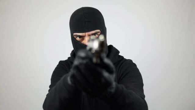 Man with black balaclava holding and pointing pistol, over white background. Crime concept