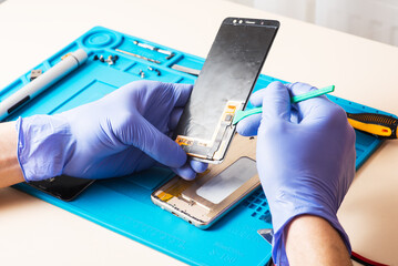 Craftsman in rubber gloves repair or service a mobile phone on a special rubber mat for repair....