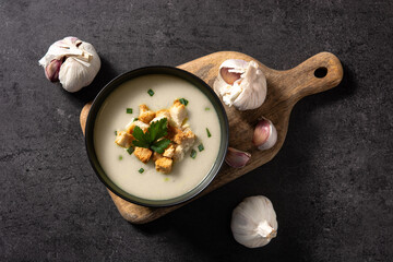 Garlic soup topped with croutons in bowl on black background