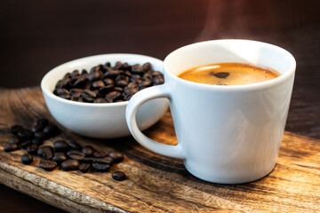 Close-up of hot black coffee in white coffee cup and roasted coffee beans in white bowl on wooden background