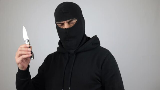 Man with black balaclava holding the knife. Bandit or thief look at the camera over white background. Crime concept