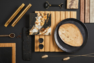 Stylish flat lay comosition of creative architect moodboard with samples of textile, paint, wooden lamella panel and marble tile. Golden, black and beige color palette. Copy space. Template.