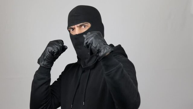 Man with black balaclava ready to fight with fist defense gesture. Bandit or thief look at the camera over white background. Crime concept