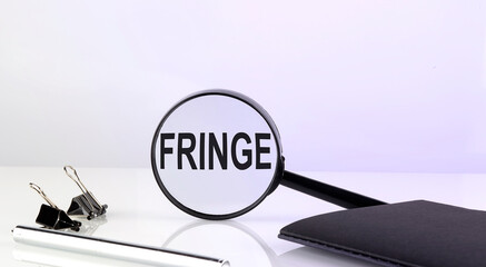 FRINGE concept. Magnifier glass with text with notebook and pen