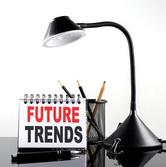 FUTURE TRENDS text on notebook with pen and table lamp on the black background